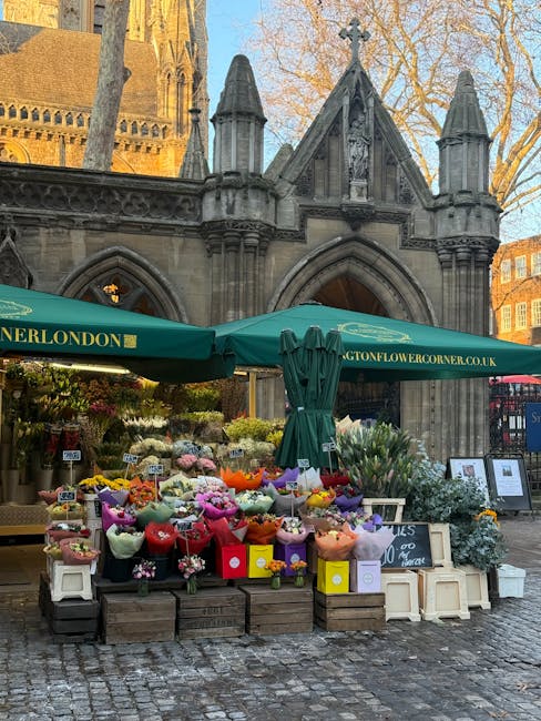 A vibrant outdoor flower stall set against a historic stone church building with gothic architectural details, including pointed arches and decorative spires. The stall features an array of colorful f
