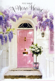 This photograph shows a lovingly decorated entrance in West Green, captured at the kind of soft, slanting light that makes colours glow. At the centre stands a pale pink front door, its paint velvety and calm, radiating warmth without shouting for attention. It is framed by luxuriant cascades of wisteria, their blossoms a gentle lavender, hanging in drifts that resemble fragrant curtains. The whitewashed wall around the door and a delicately painted shutter catch the sun, creating a canvas of quiet light into which the flowers and door seem to sink. Resting directly on the doorstep is a stylish grey metal bucket, used as a planter for an abundant arrangement of white and cream roses. The roses are large and fully open, with velvety petals layered in spirals, and are accented by soft, natural greenery that peeks between them, offering texture and a hint of woodland freshness. Tied neatly around the bucket is a soft pink ribbon, its bow relaxed but precise, picking up the colour of the door and suggesting that a professional florist has taken care with every detail. The overall atmosphere is one of serene joy, like arriving at a freshly painted house near Lordship Lane on the very first day of moving in. You can almost imagine the gentle mingling scents of wisteria and rose greeting you at nose level as you turn the key, making this arrangement perfect for celebrating a new home with understated elegance, affection, and the comforting sense that this doorway will hold many happy arrivals to come.